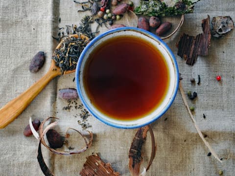 Eine Tasse Tee mit einem blauen Rand und verschiedenen Kräutern und Gewürzen drum herum.