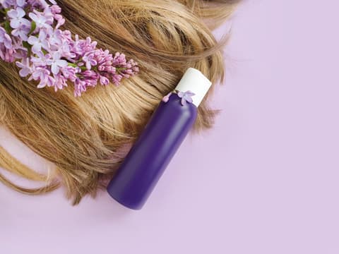 Das beste Drogerie Shampoo ist gar nicht so leicht zu finden. Haare einer Frau liegen mit Orchideen und einer lila Flasche auf einem rosafarbenen Hintergrund.