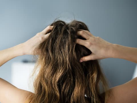 Frau von hinten fasst sich mit beiden Händen in die Haare an den Kopf.