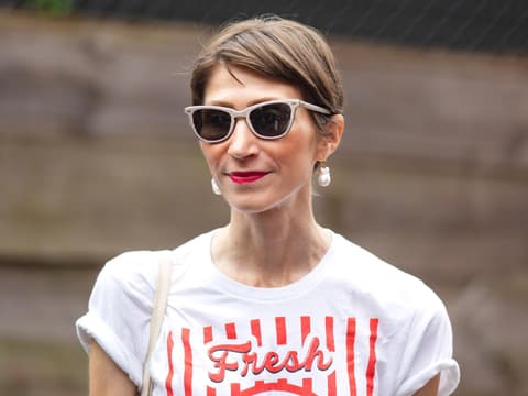 Frau mit braunhaarigem Kurzhaarschnitt, einer beigen Sonnenbrille und roten Lippen.