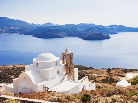 Eine griechische Kapelle mit dem Meer und Landschaft im Hintergrund.