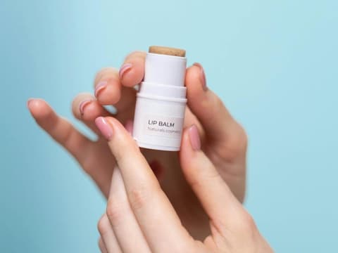 Ein Lip Balm wird in der Hand vor einem hellblauen Hintergrund gehalten.