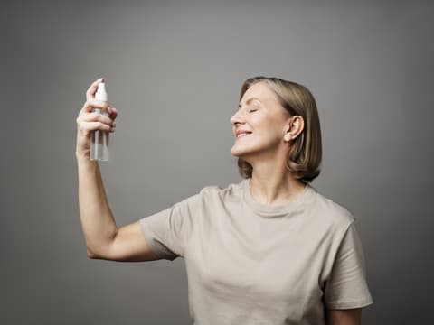 Frau sprüht Gesichtsspray in ihr Gesicht.