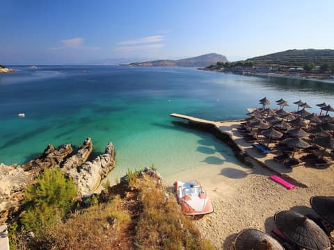 Ein Blick auf den Strand und das Meer von Ksamil mit Sonnenschirmen und Liegen.