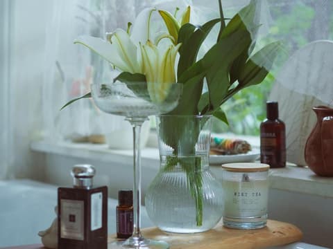 Eine Vase mit Lilien steht auf einem Brett, das über der Badewanne liegt, daneben eine Kerze und ein Parfum.
