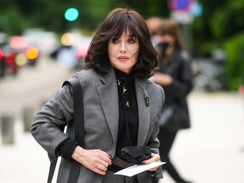 Frisuren mit Pony sehen ab 50 besonders gut aus. Frau mit dunklem Longbob und Pony trägt eine schwarze Bluse und einen grauen Blazer.