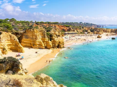 Ein Strand mit Urlaubern, türkisblauem Wasser und Klippen.