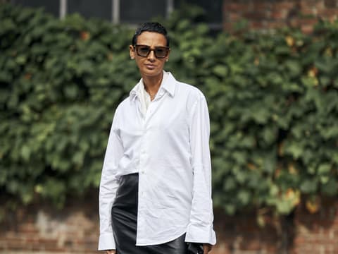 Frau mit kurzen Haaren trägt eine weiße Bluse, einen kurzen Lederrock und Loafer mit weißen Socken.
