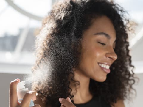 Frau sprüht Spray in die Haare