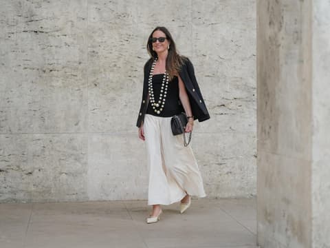 Maxi-Röcke im Boho-Stil liegen wieder total im Trend. Frau trägt einen weißen Maxi-Rock im Boho-Stil mit einem schwarzen Top und Blazer und zwei großen Perlenketten.