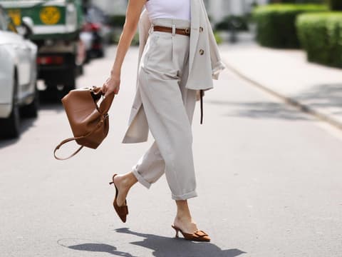 Sommerschuhe wie Kitten Heels sind Trend 2025. Frau mit rotem Lippenstift trägt ein weißes Top, eine beige Chinohose und Kitten Heals auf der Straße.