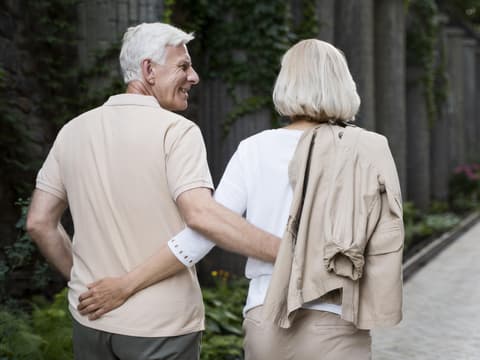 Wir verraten, welche 10 Angewohnheiten und Verhaltensweisen bei glücklichen Paaren zu erkennen sind, die auch im Alter noch zufrieden sind. Älteres Pärchen spaziert Arm in Arm.