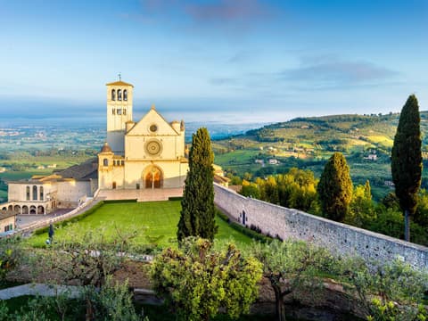 Basilika von Assisi auf einem Hügel mit viel Grünfläche drum herum.