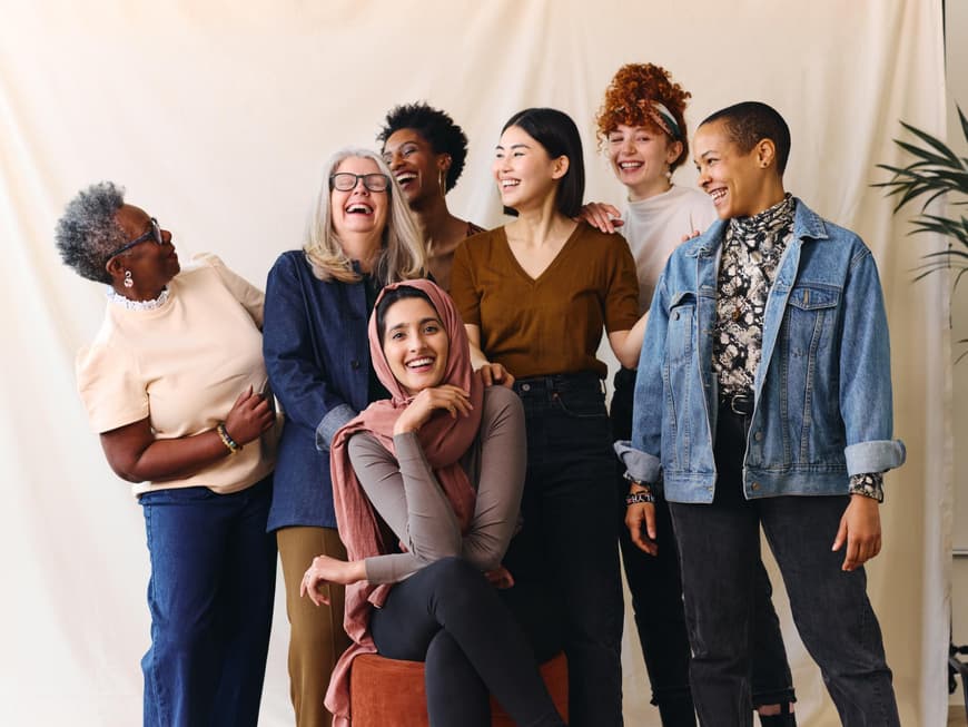Eine Gruppe Frauen steht vor einem weißen Hintergrund und lacht