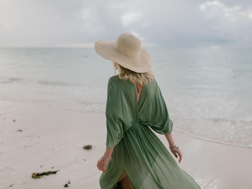 Frau mit grünem Kleid und Strohhut am Strand