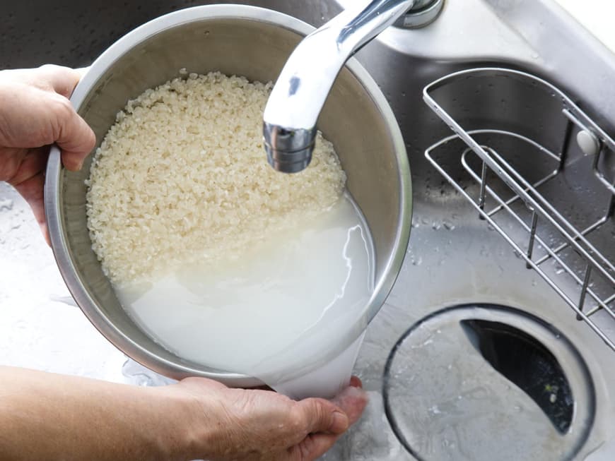 Frau schüttet Reiswasser in den Abfluss