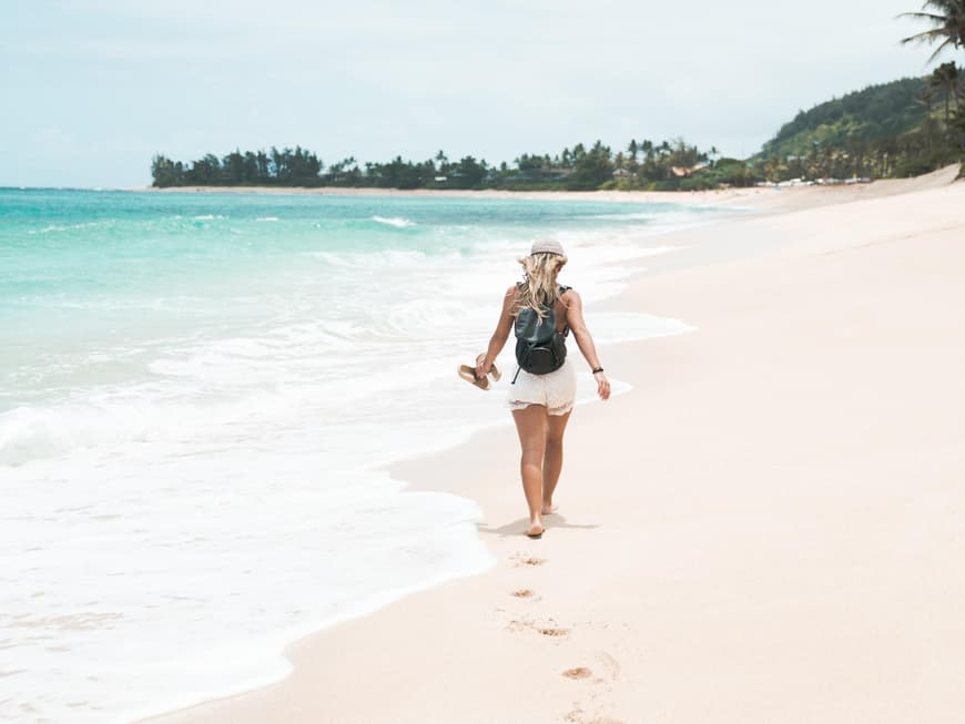 Frau mit weißen Shorts und Hut läuft am Strand