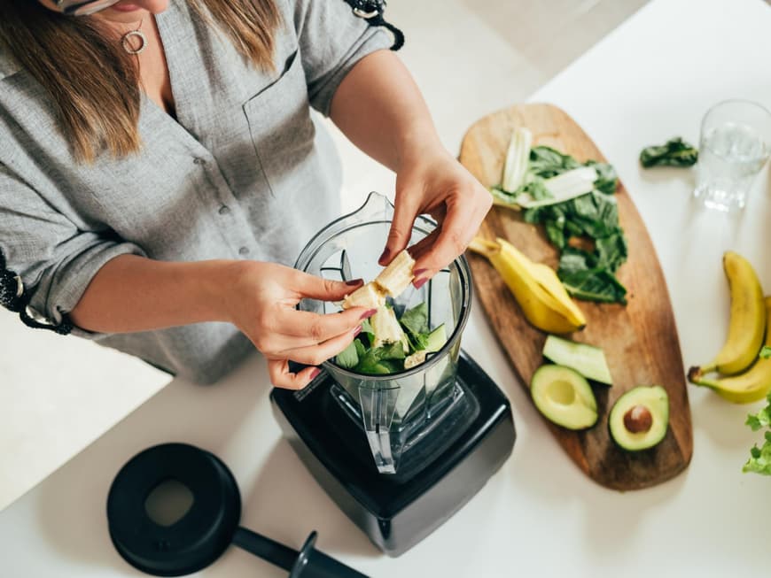Frau legt Zutaten in einen Mixer