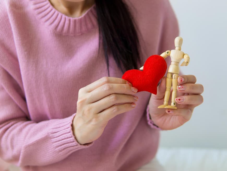 Gesundheit Frau im rosafarbenen Pullover hält ein Herz neben eine Holzfigur