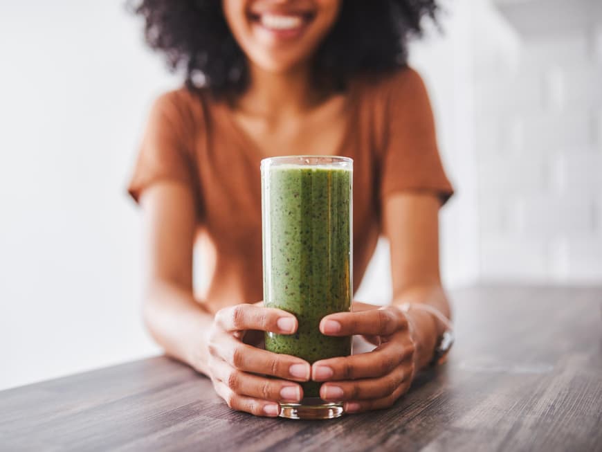 Frau hält einen Glas mit einem grünen Smoothie in der Hand