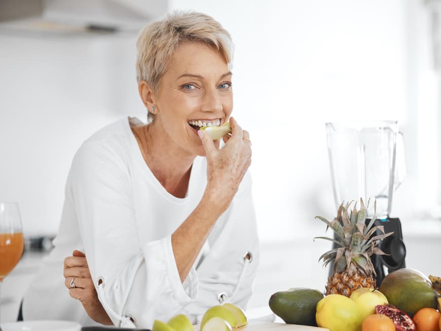 Frau mittleren Alters isst ein Stück Obst in der Küche