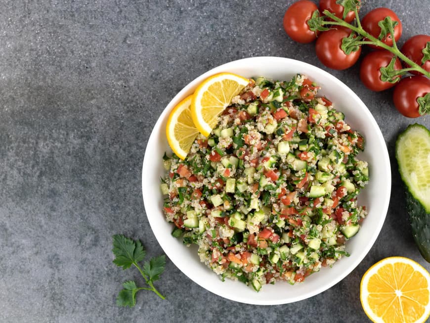 Teller mit Quinoa-Salat, Gurke, Tomaten und Zitrone steht auf einem Tisch