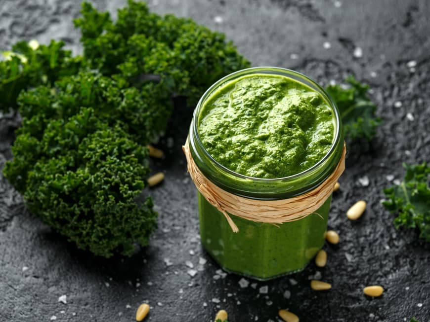 Ein Glas Grünkohl-Pesto mit Pinienkernen steht auf einem grauen Tisch