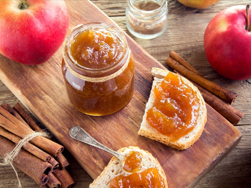 Rezept für weihnachtliche Bratapfelmarmelade Glas Marmelade mit Zimt streht auf einem Holztisch