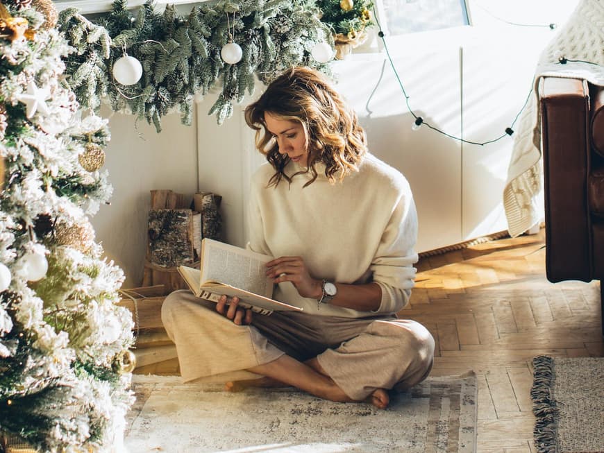 Frau liest ein Buch unter dem Weihnachtsbaum.