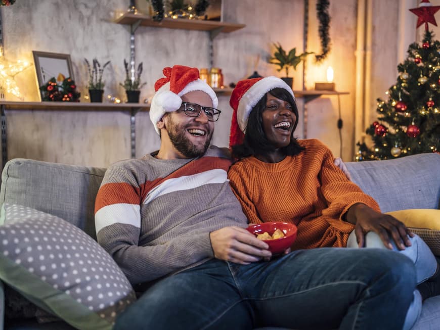 Glückliches Paar sitzt auf der Couch und guckt einen Weihnachtsfilm