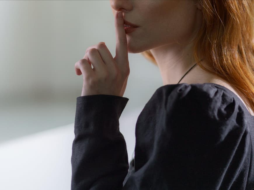 Frau hält ihren Zeigefinger vor ihren Lippen