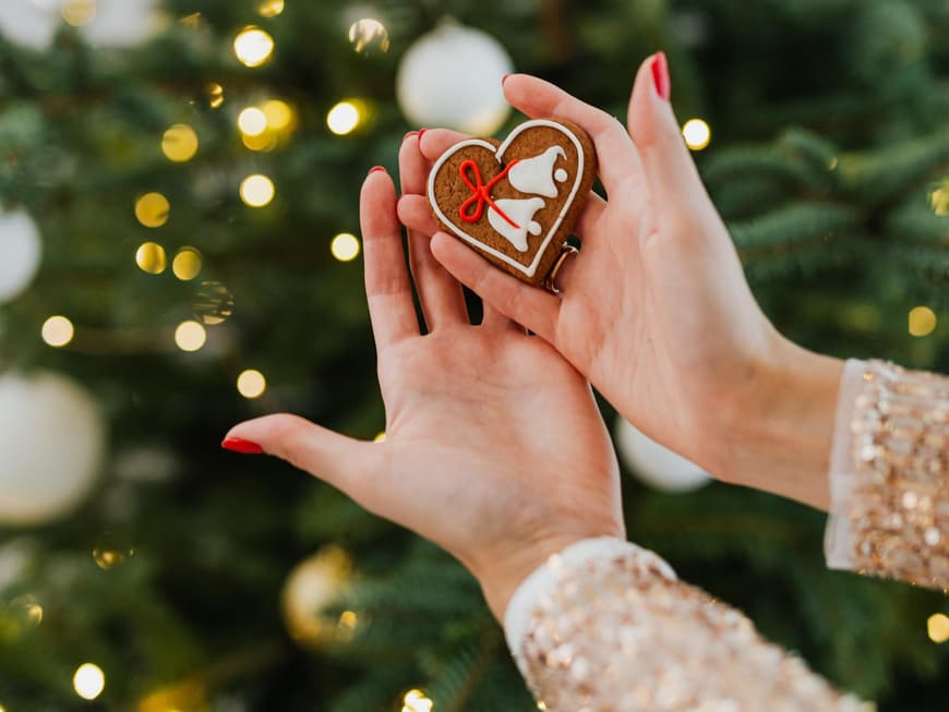 Frau hält ein Lebkuchenherz vor einem geschmückten Tannenbaum