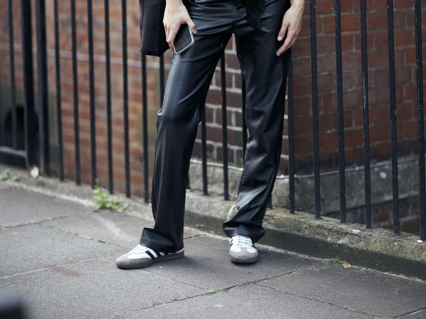 Frau trägt auf London Fashion Week weiße Retro-Sneaker und Lederhose Frau trägt auf London Fashion Week weiße Retro-Sneaker und Lederhose
