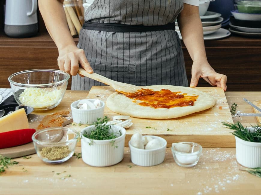 Frau belegt einen Pizzateig