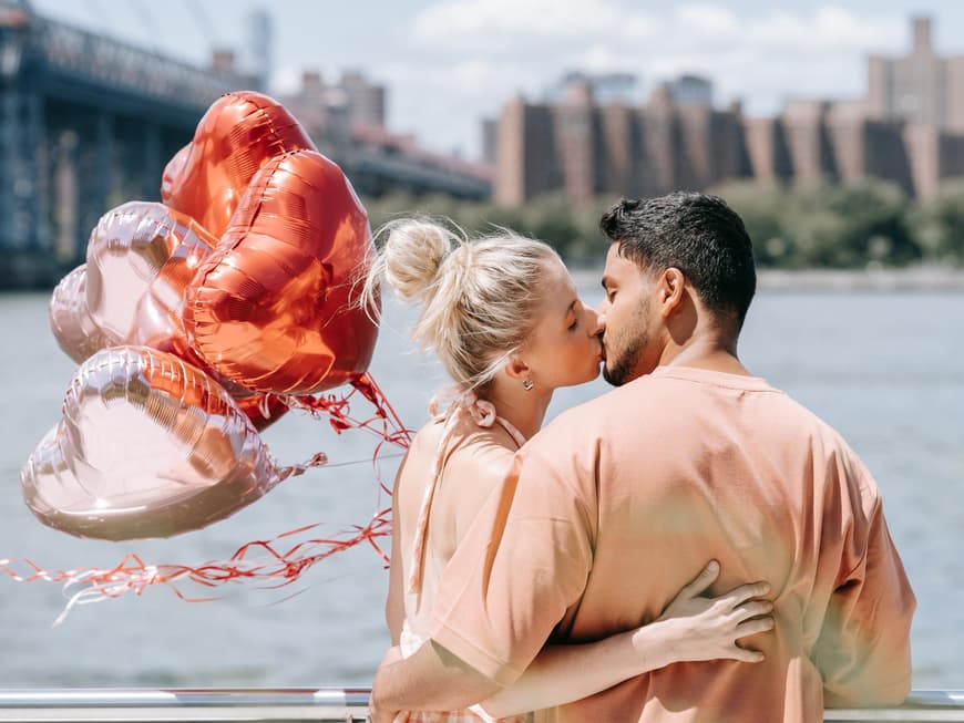 Verliebtes Paar küsst sich am Wasser und hält Herzluftballons in der Hand