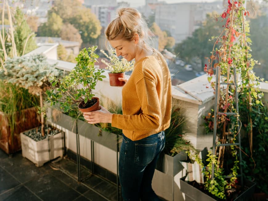 Frau steht auf einem Balkon und hält Pflanzen in der Hand