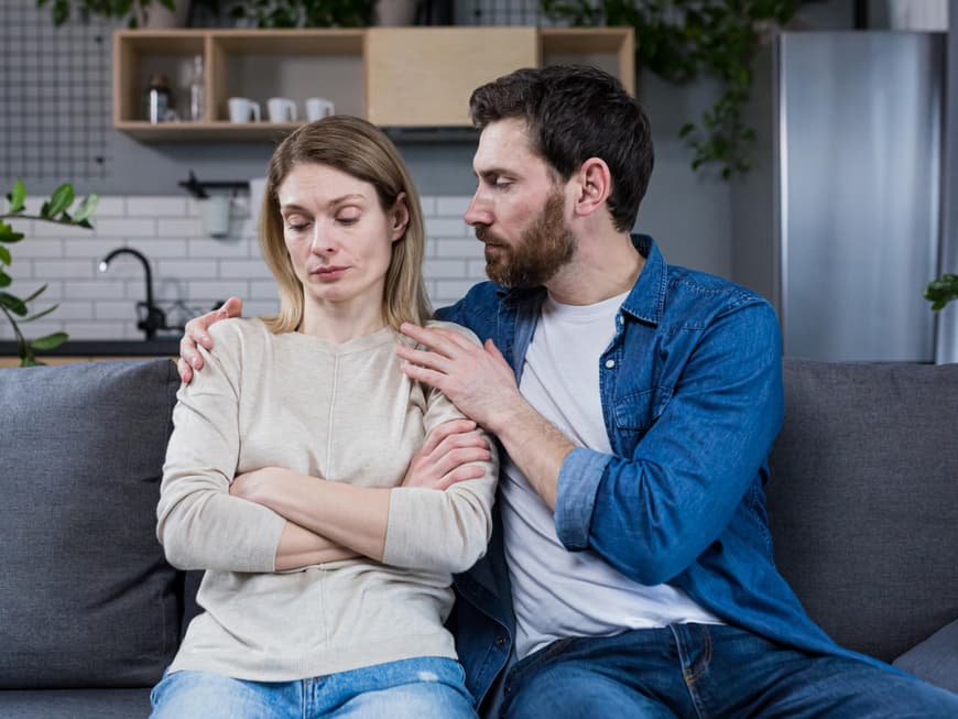 Paar sitzt auf dem Sofa, der Mann umarmt die Frau
