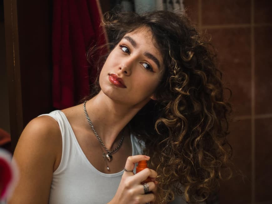 Frau mit Locken sprüht Spray in ihr Haar Frau mit Locken sprüht Spray in ihr Haar