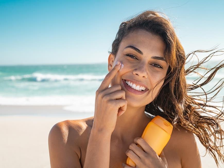 Frau am Strand trägst Sonnencreme auf ihr Gesicht auf