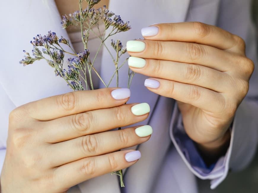 Hände mit bunten Fingernägeln und Blumen in der Hand.