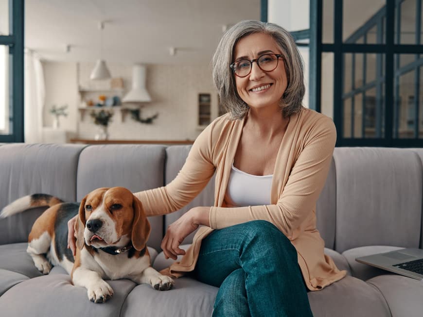 Frau mit grauen Haaren und einem Hund auf dem Sofa.