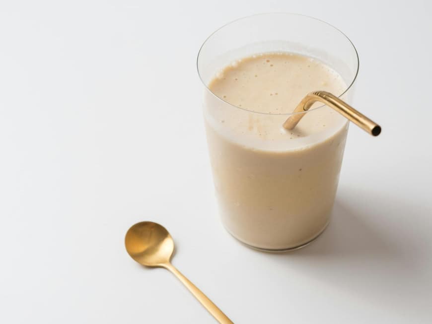 Ein cremiger Shake im Glas mit goldenem Strohhalm.