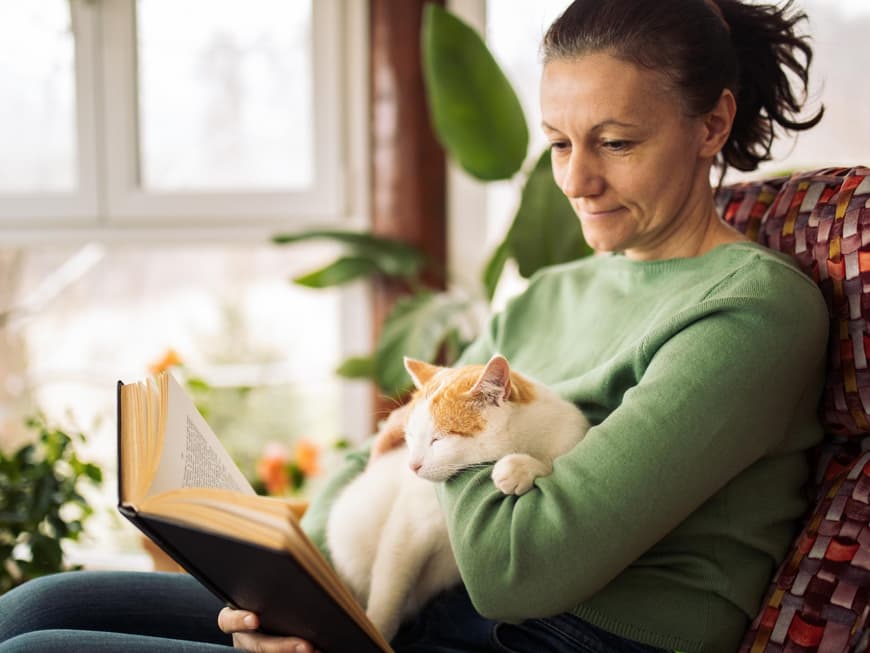 Frau mit Katze auf dem Schoß am Lesen.