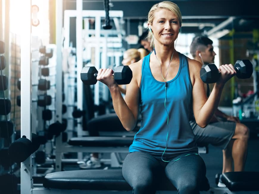 Frau mit zwei Hanteln trainiert ihren Bizeps im Fitnessstudio.
