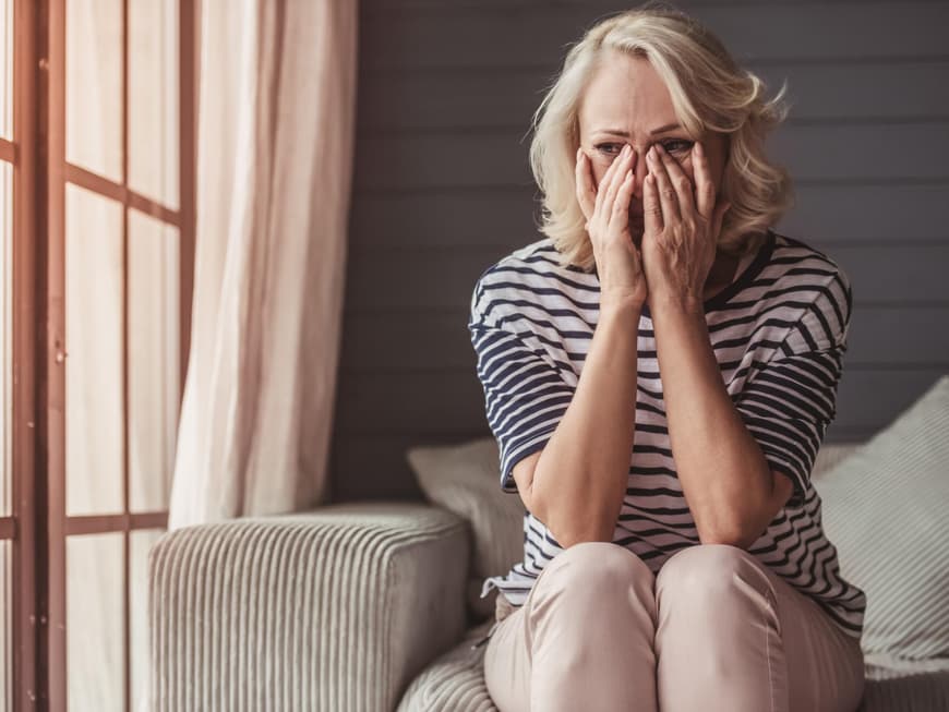 Frau sitzt auf dem Sofa und hält die Hände ins Gesicht.