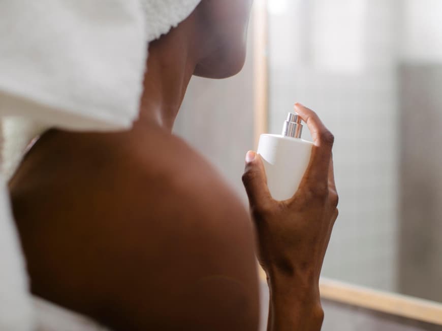 Frau sprüht nach dem Duschen Parfum auf.