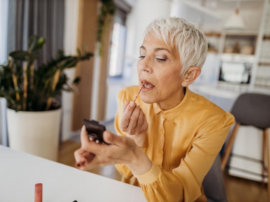 Frozen Glow ist ein neuer Make-up-Trend für den Winter. Ältere Frau schminkt sich die Lippen mit einem kleinen Spiegel.