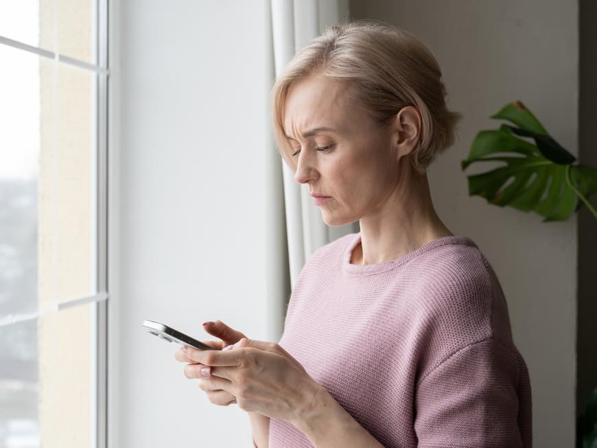 Es gibt verschiedene Anzeichen dafür, dass dein Handy ausspioniert wird. Frau guckt skeptisch auf ihr Handy.