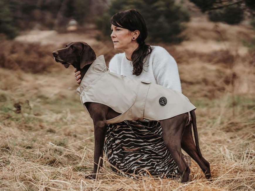 Frau hockt neben einem Hund mit Regenmantel.