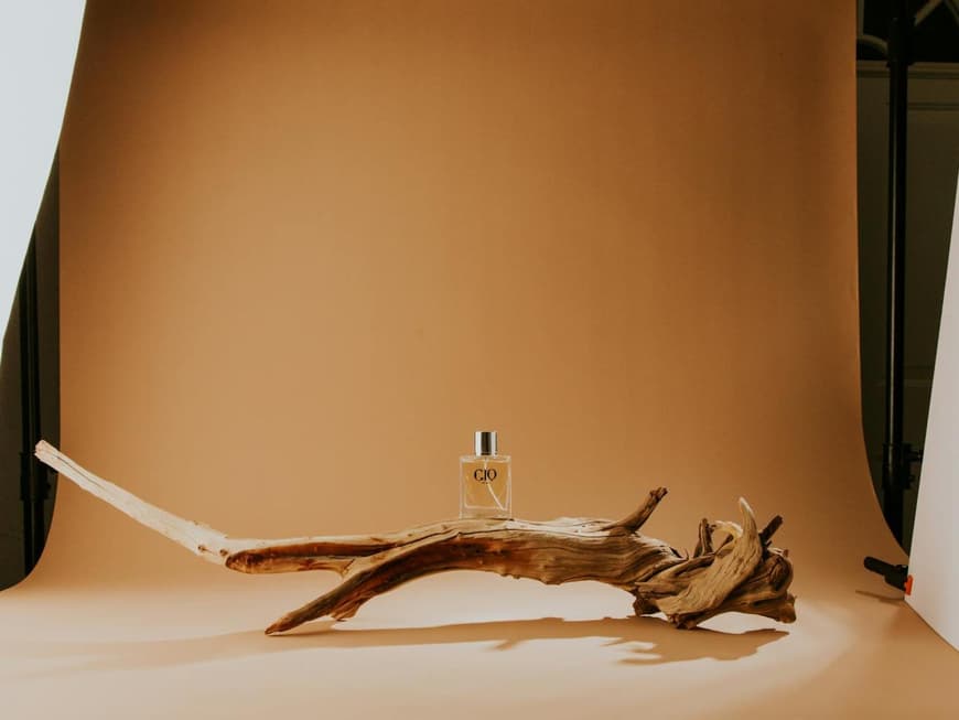 Parfum Flakon auf einem Baumstamm vor einem bräunlichen Hintergrund.